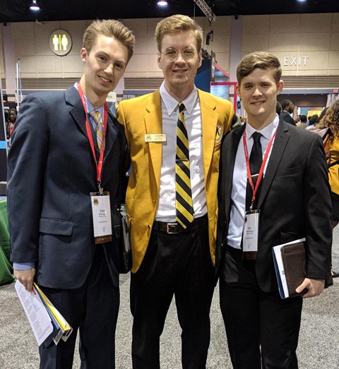 Three students standing together with suitcoats and ties at conference.