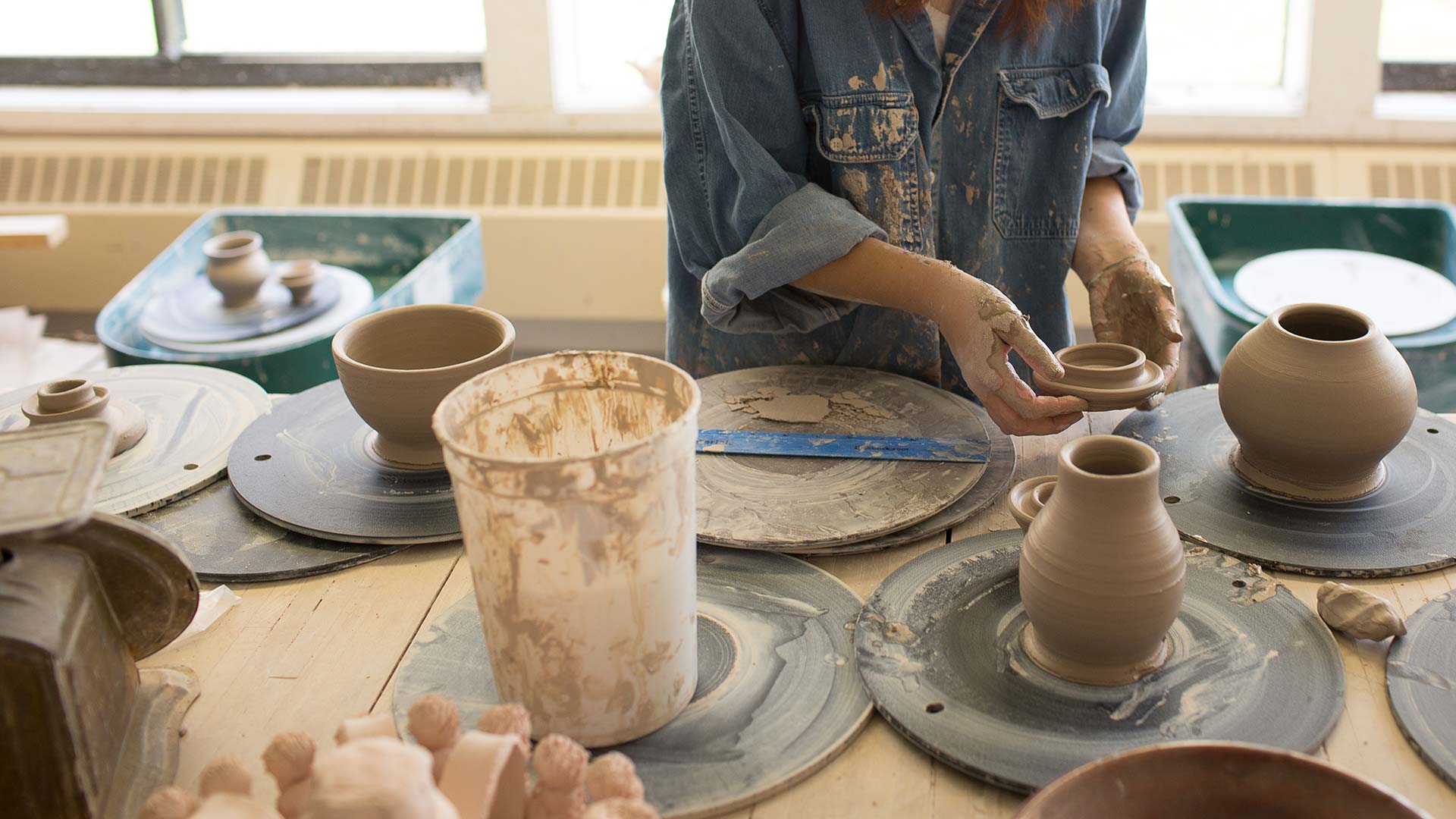 Studio art major student arranging pottery on table.