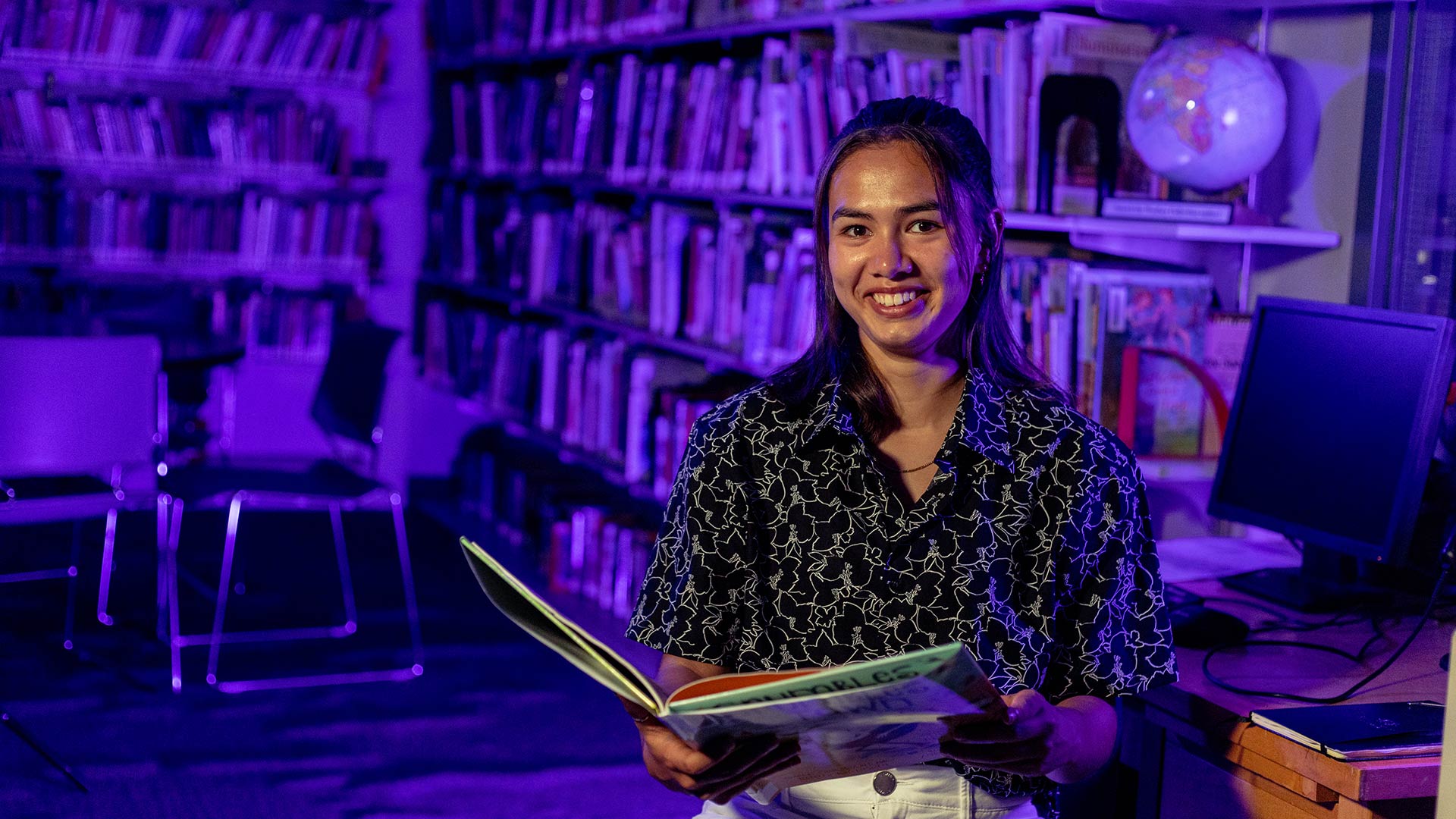 student smiling while reading book in school library