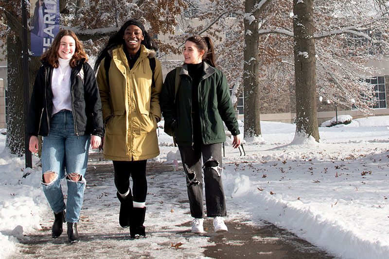 Three students laughing as they walk across a snowy campus