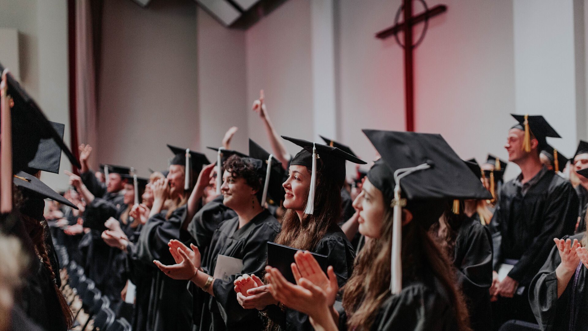 Students in graduation robes clapping at Commencement