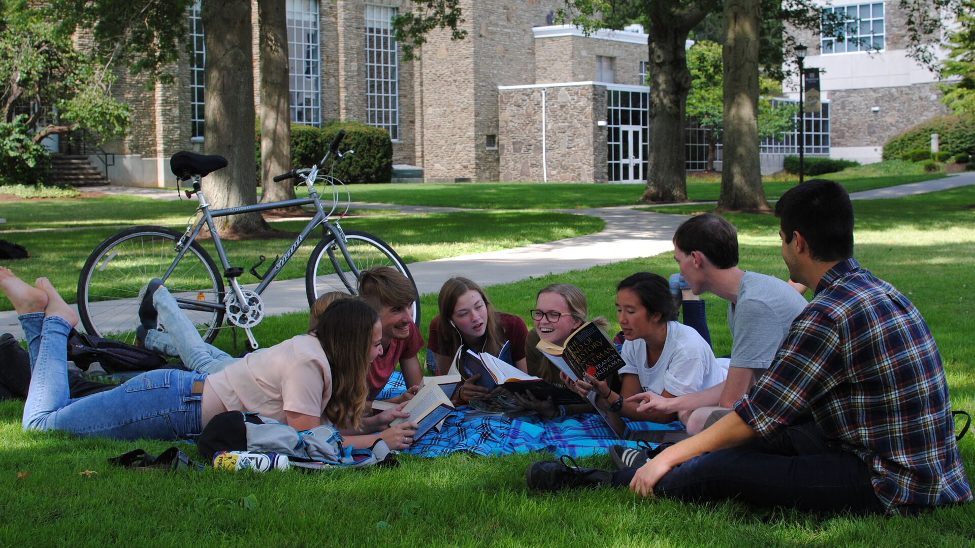 Student gathered on a blanket sharing a book together on Houghton's campus.