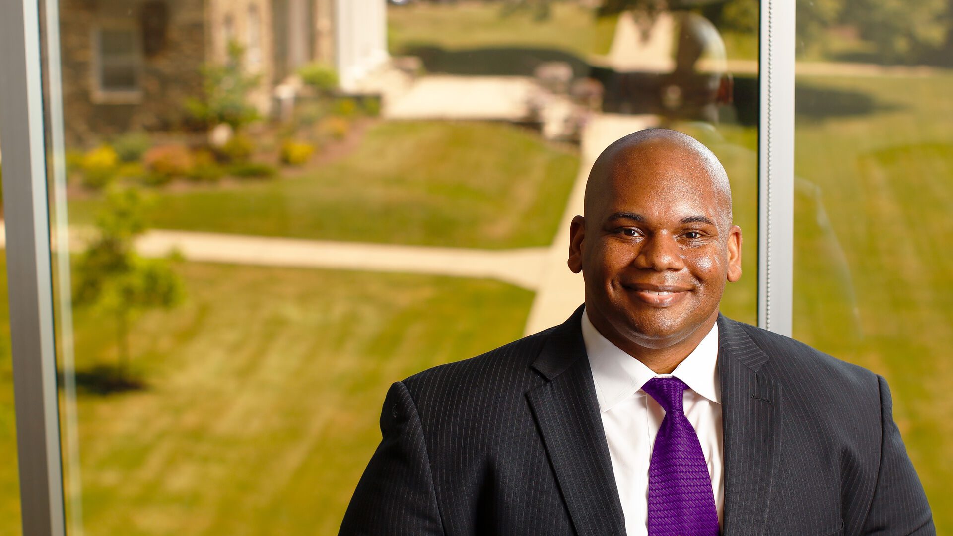 President Lewis on Houghton's campus wearing pinstripe suit and purple tie.