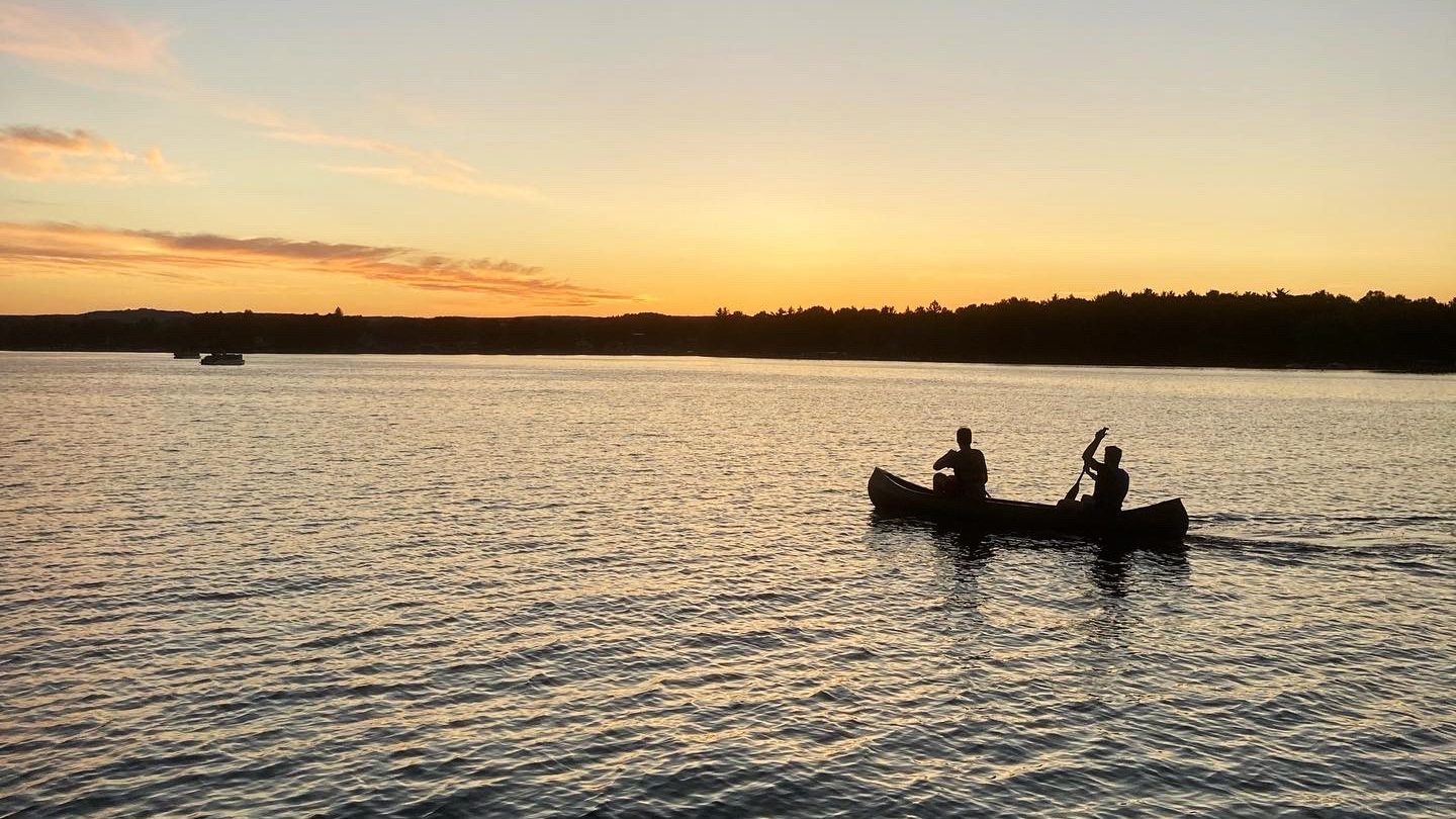 Two students in canoe paddling on lake during sunset.