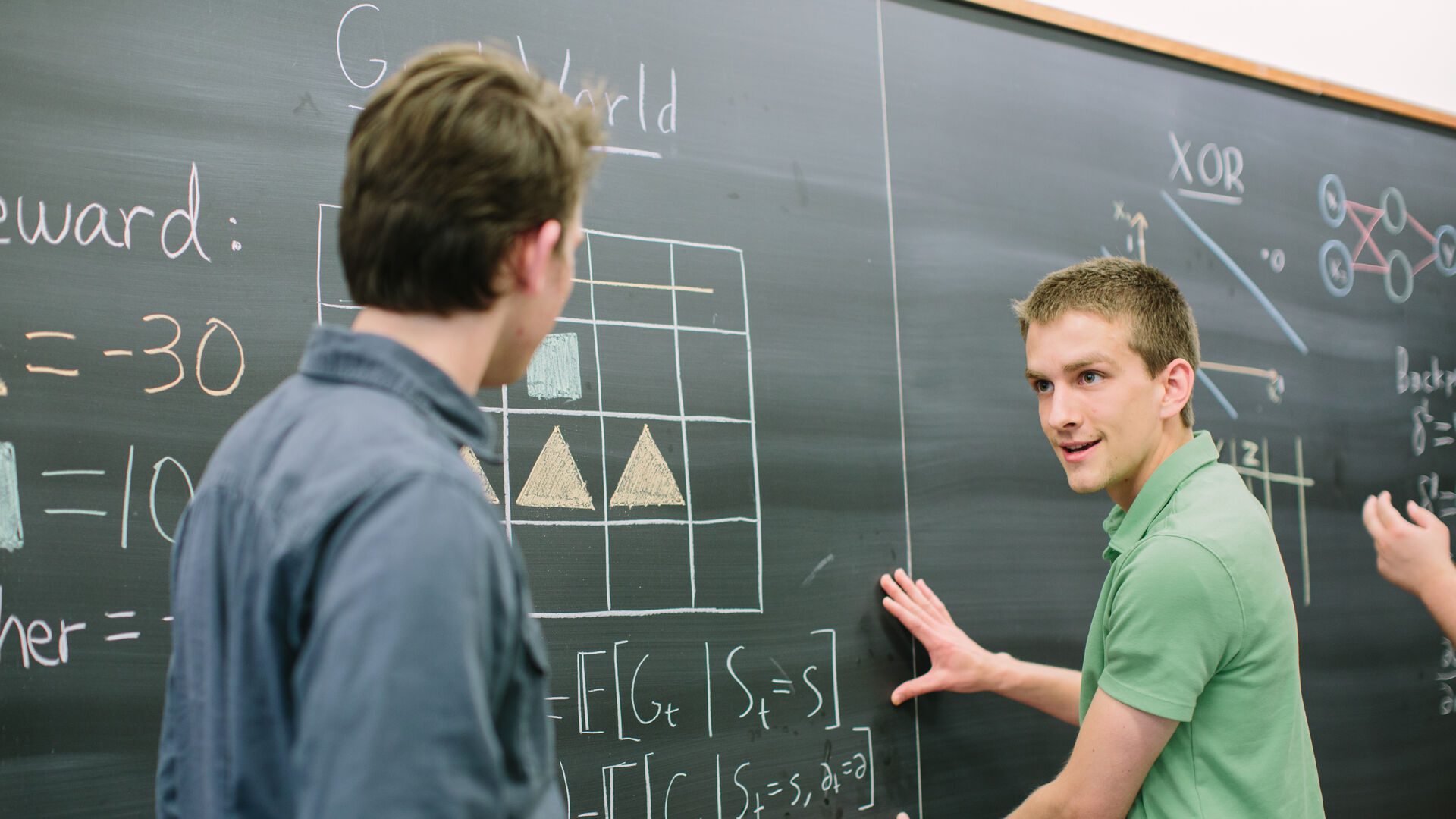 Two Houghton computer science students working through problem at the chalkboard.