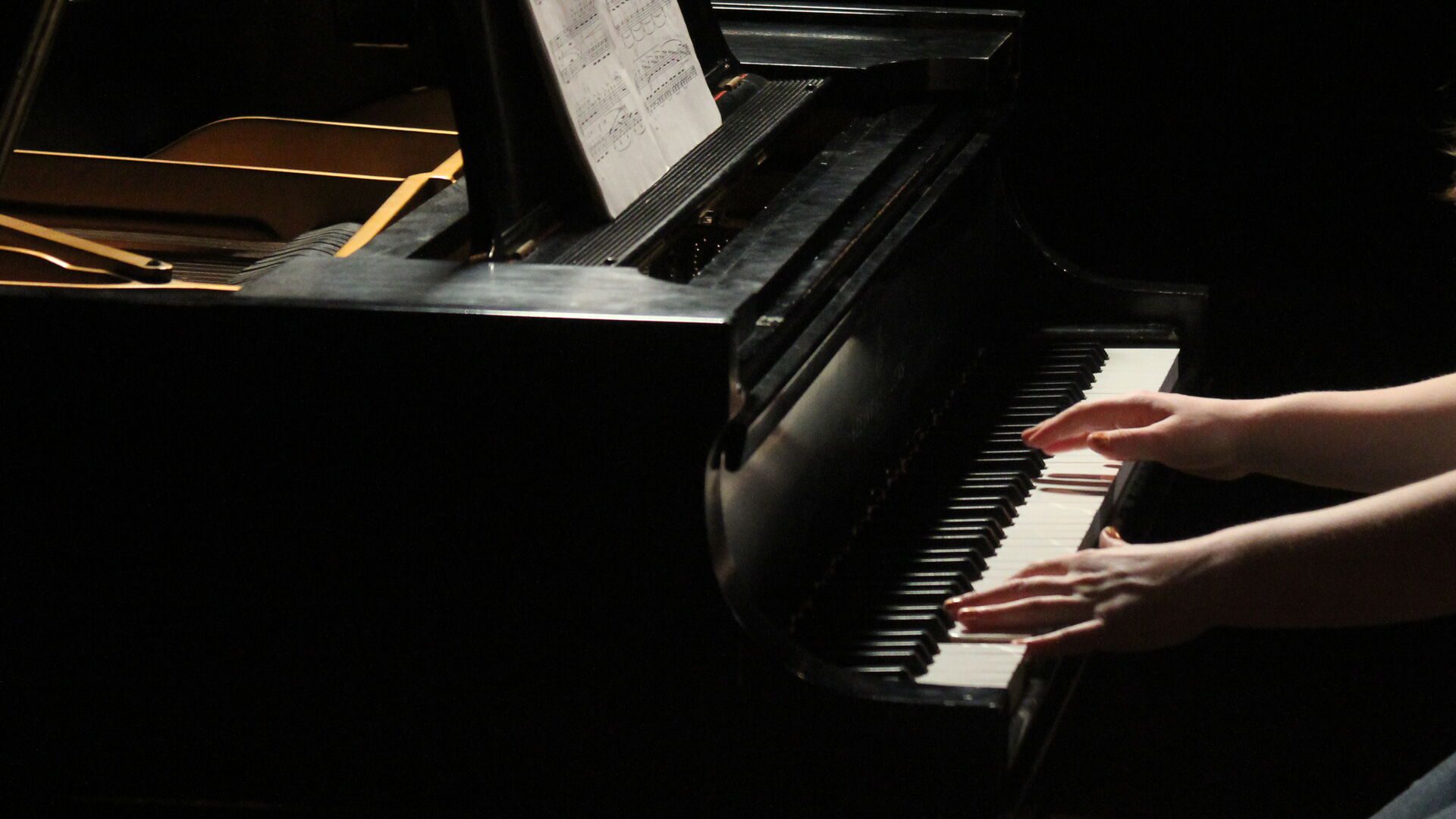 Student playing the piano on a dimmed stage.