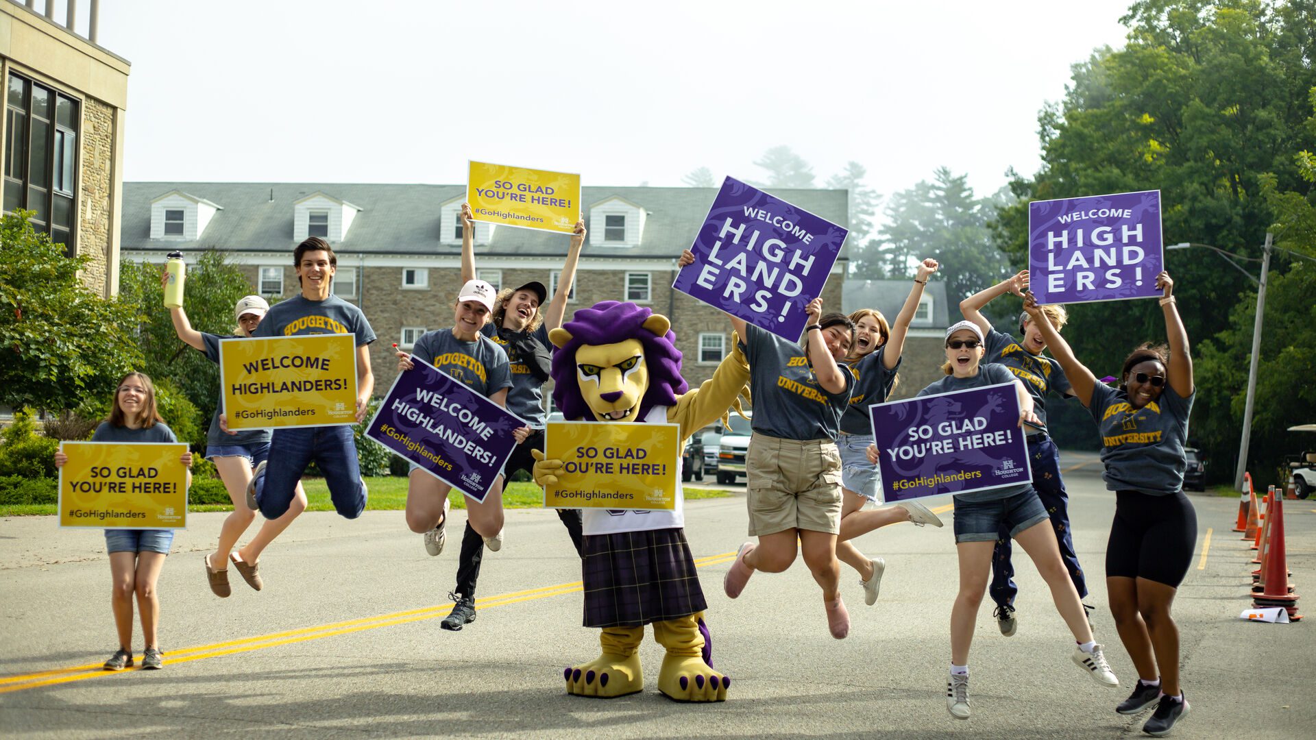Group of Houghton students holding signs and jumping in the air welcoming the incoming class during move-in.