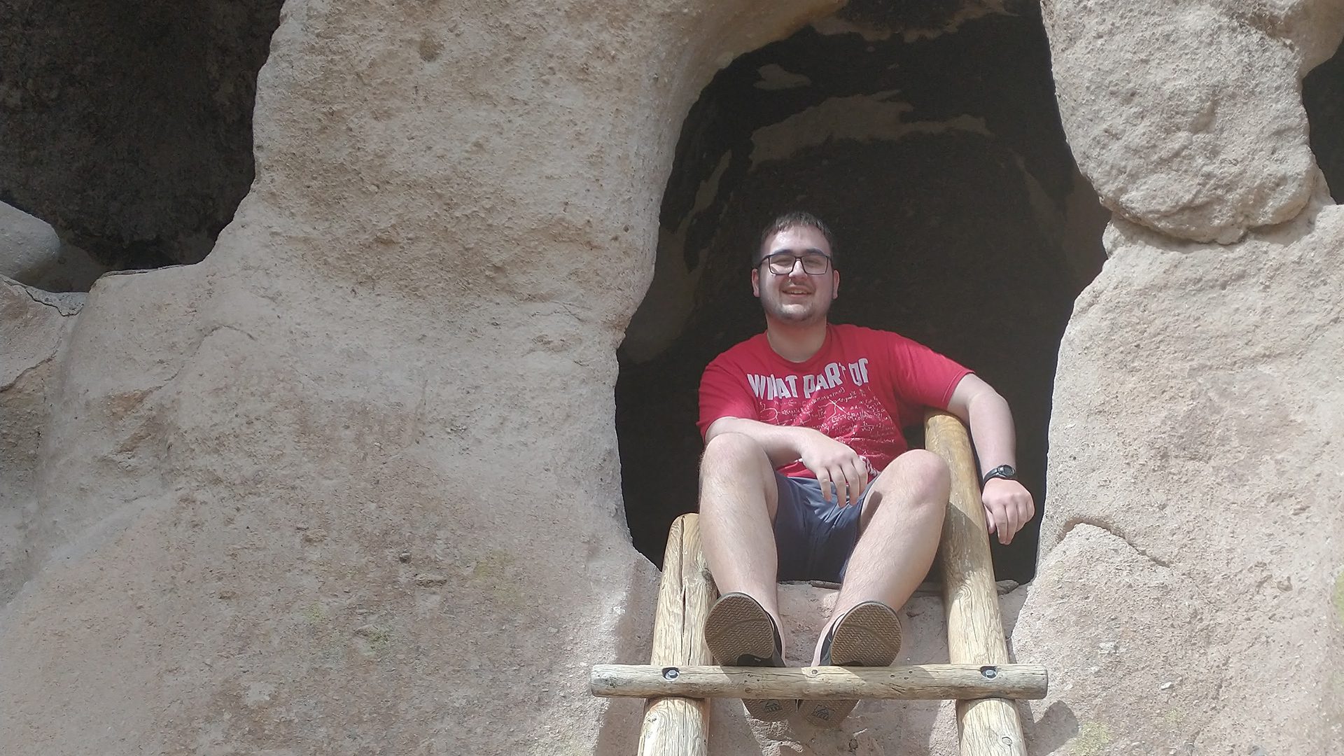 Houghton student Tim Ockrin sitting at the top of ladder at the Bandelier National Monument.