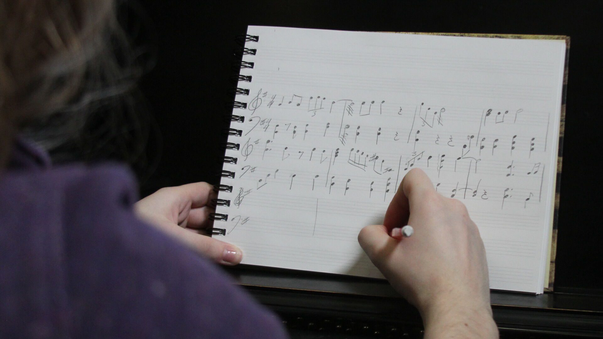 Student hand writing music on composition notebook.