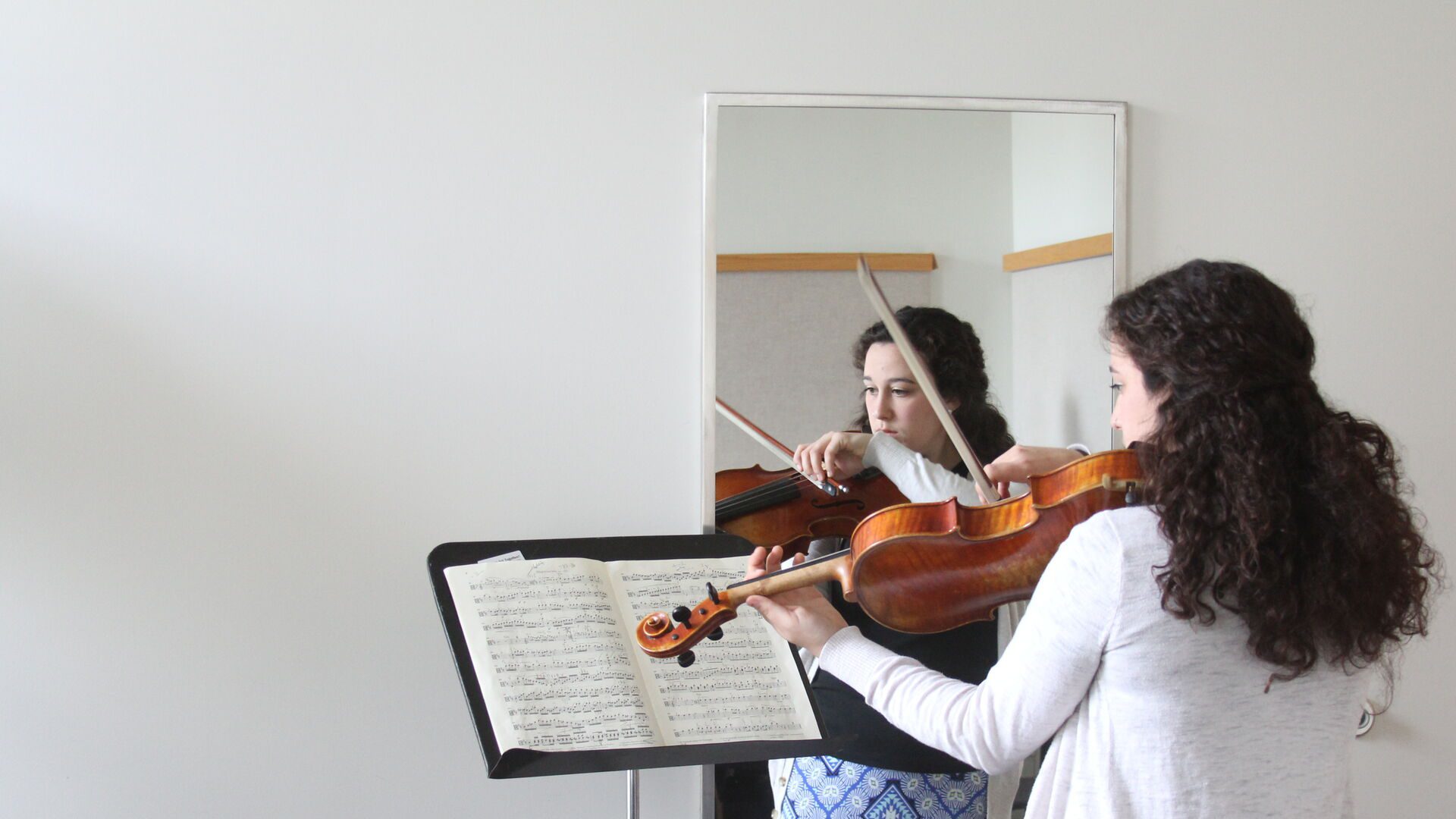 Houghton student playing her violin while looking the mirror.