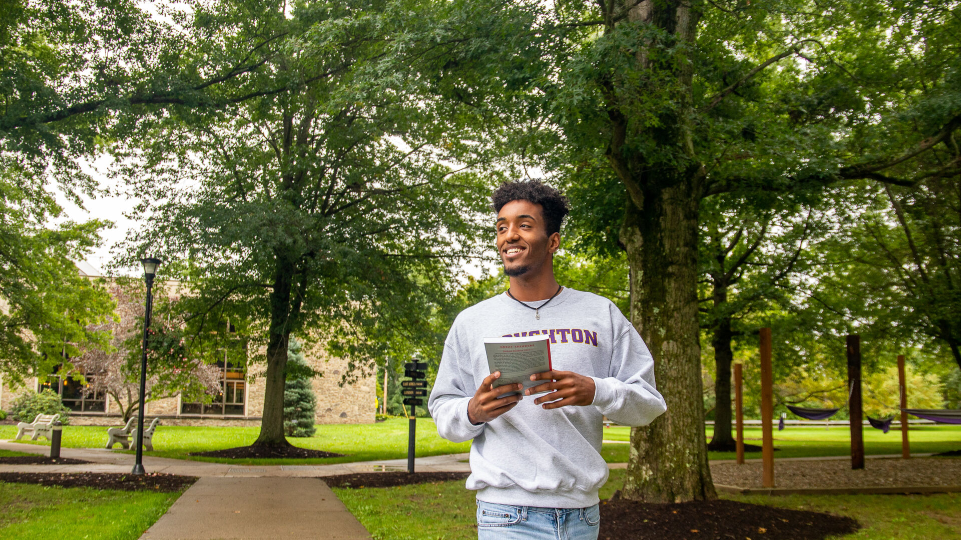 Houghton student walking on campus holding book and wearing Houghton sweatshirt.