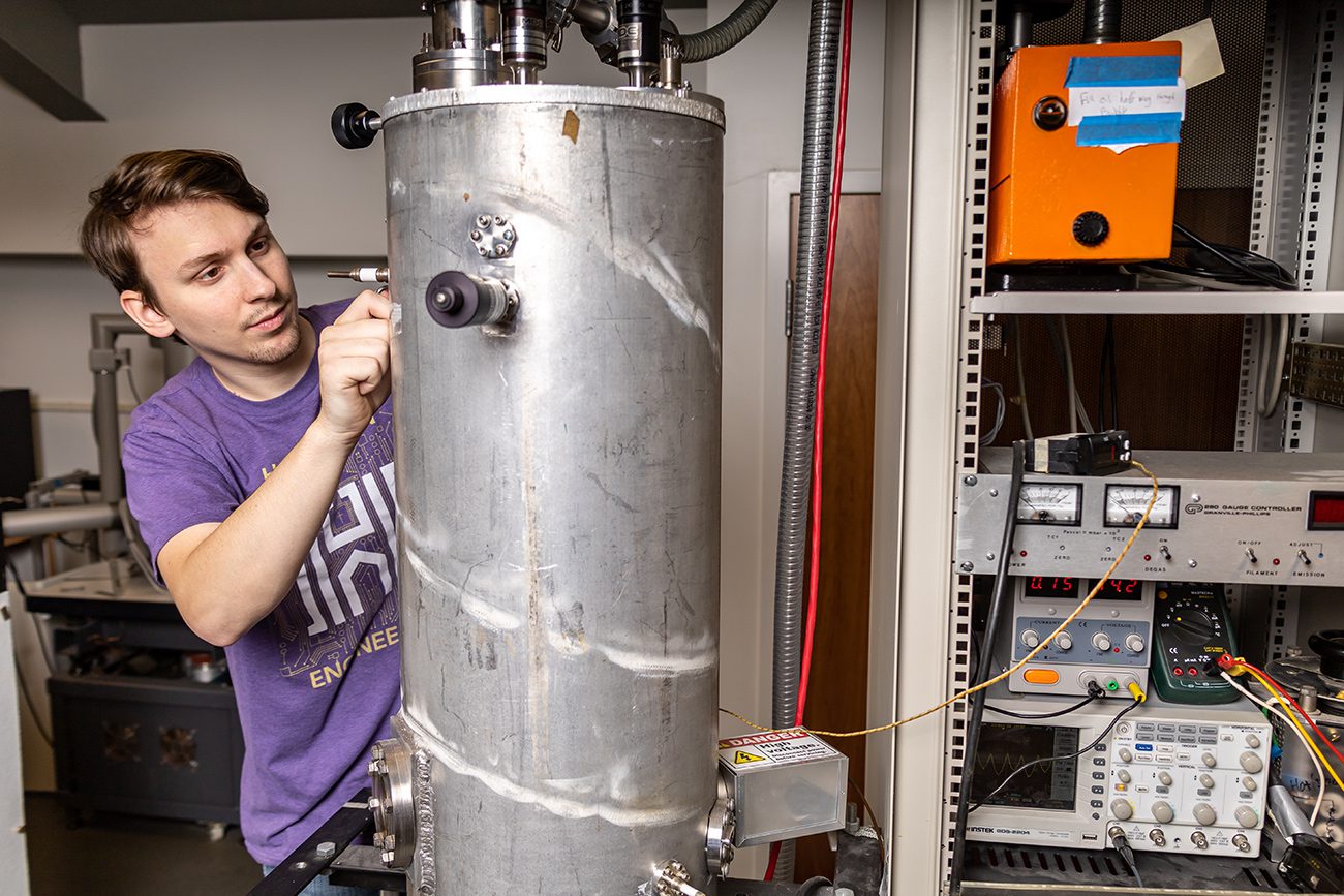 Houghton physics student working with thin film deposition chamber in lab.