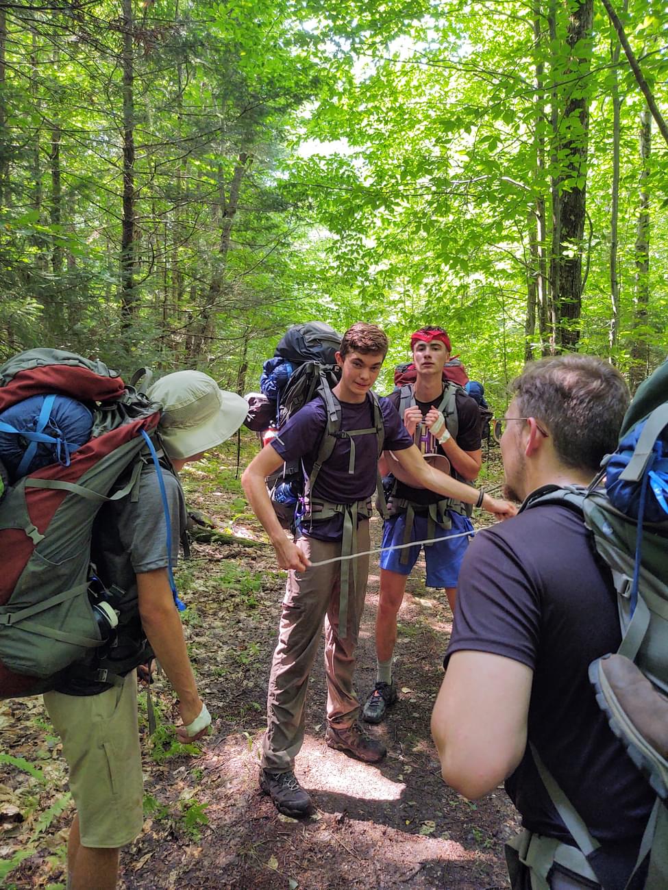 Houghton students standing together in forest with backpack gear.