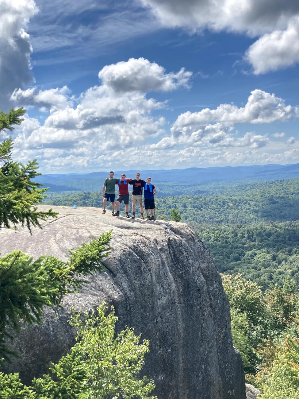 Four students standing on mountain top on beautiful sunny day.
