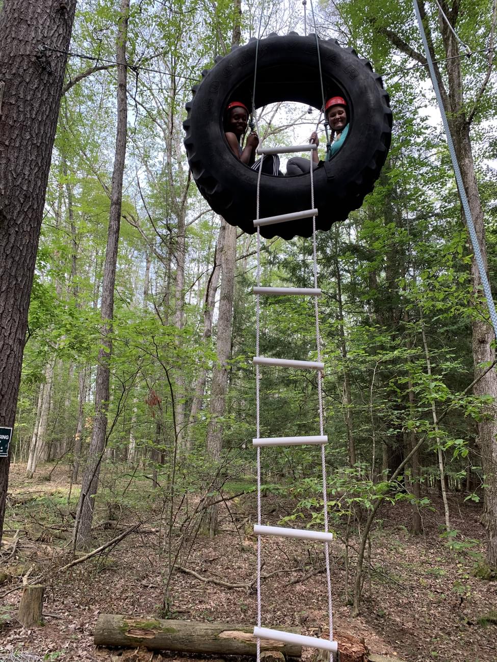 Two students in hanging tire on ropes course.