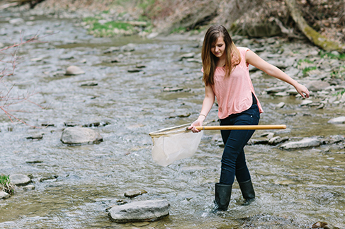 Houghton Biology student walking with net wearing boots in river.