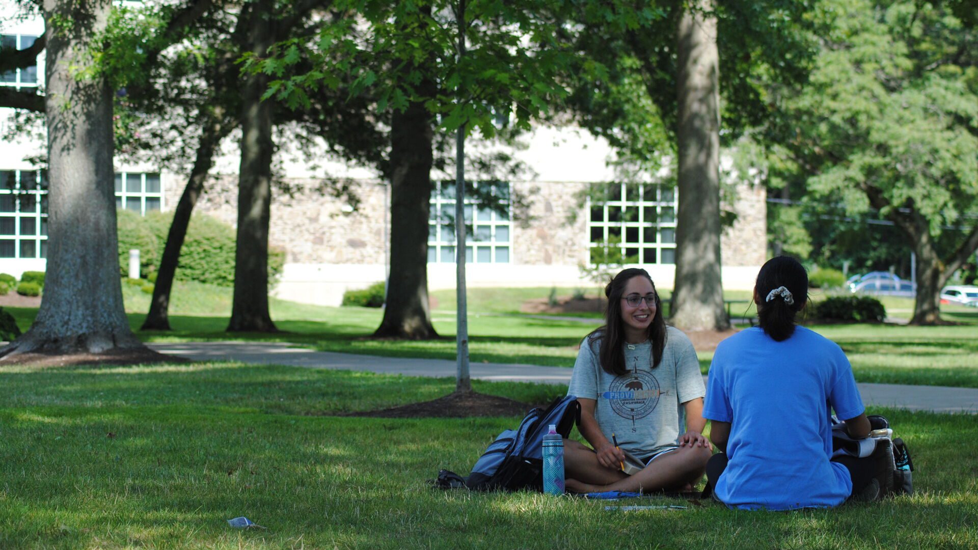 Two Houghton students sitting on campus lawn talking.