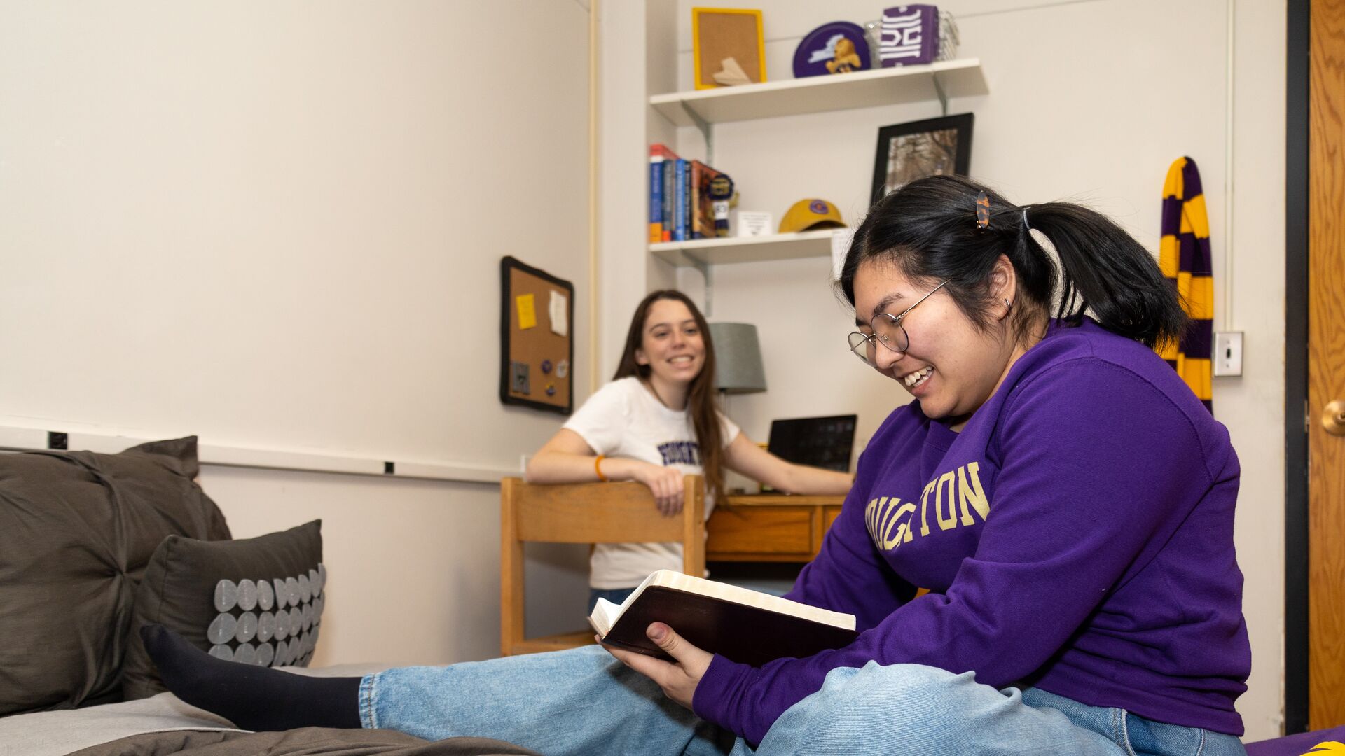 Two Houghton students sitting in dorm room reading and hanging out together.