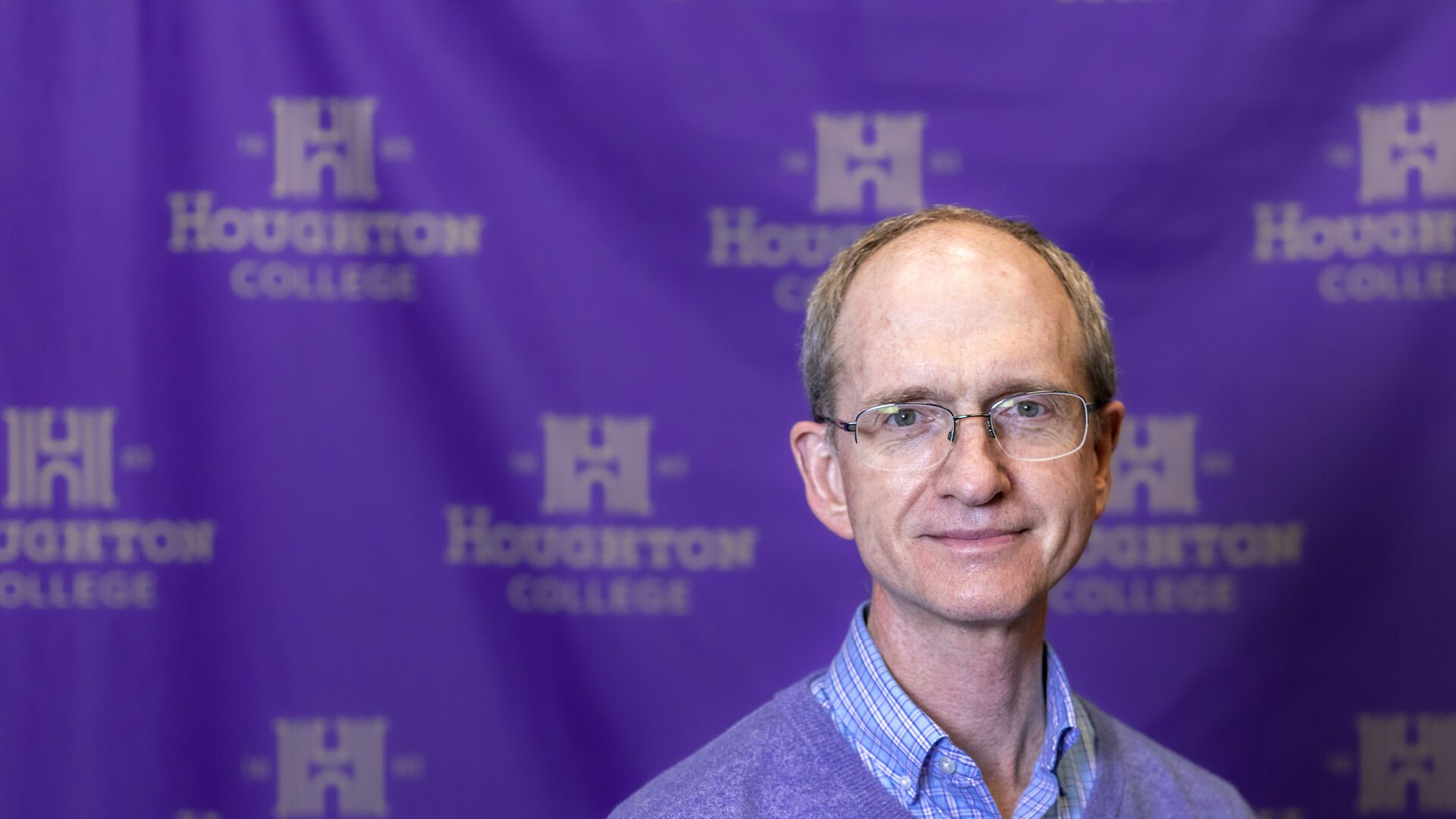 Houghton Professor Marcus Dean standing in front of Houghton University step and repeat banner.