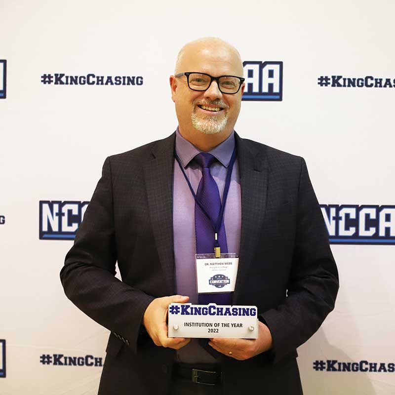 Matthew Webb standing with #kingchasing award in front of step and repeat banner.