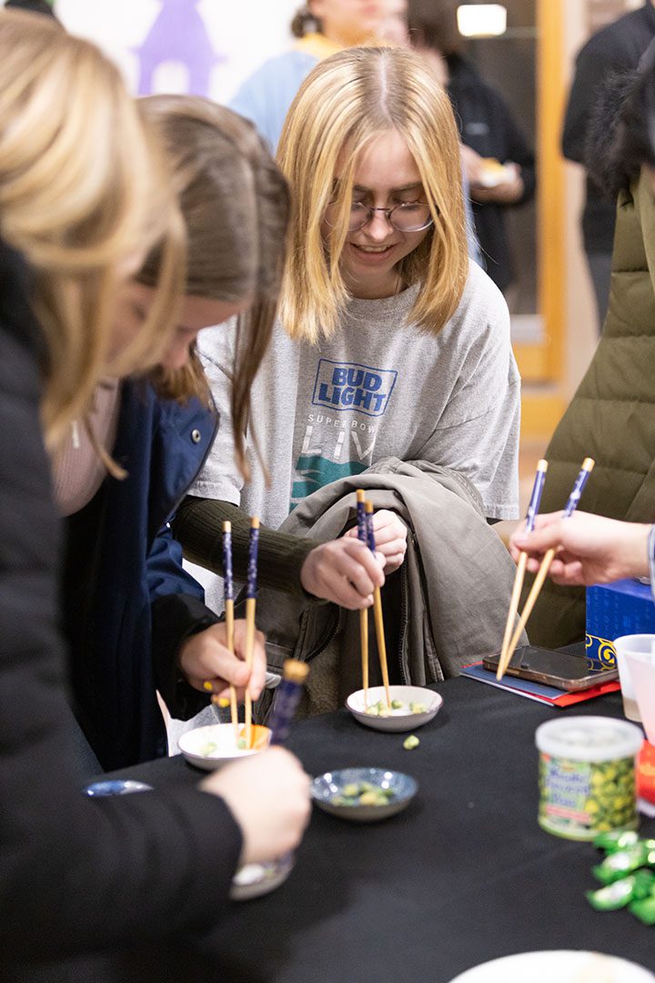 Three Houghton students eating with chopsticks at the multicultural around the world event.