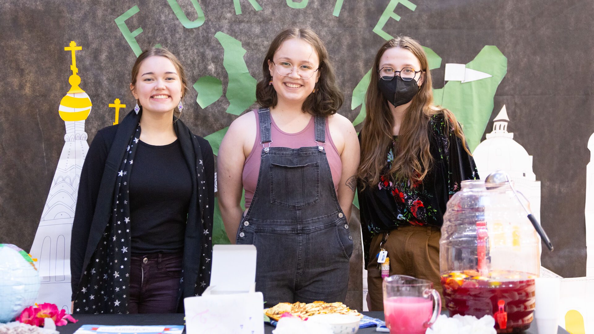 Three Houghton students standing at the Europe table at the multicultural around the world event.