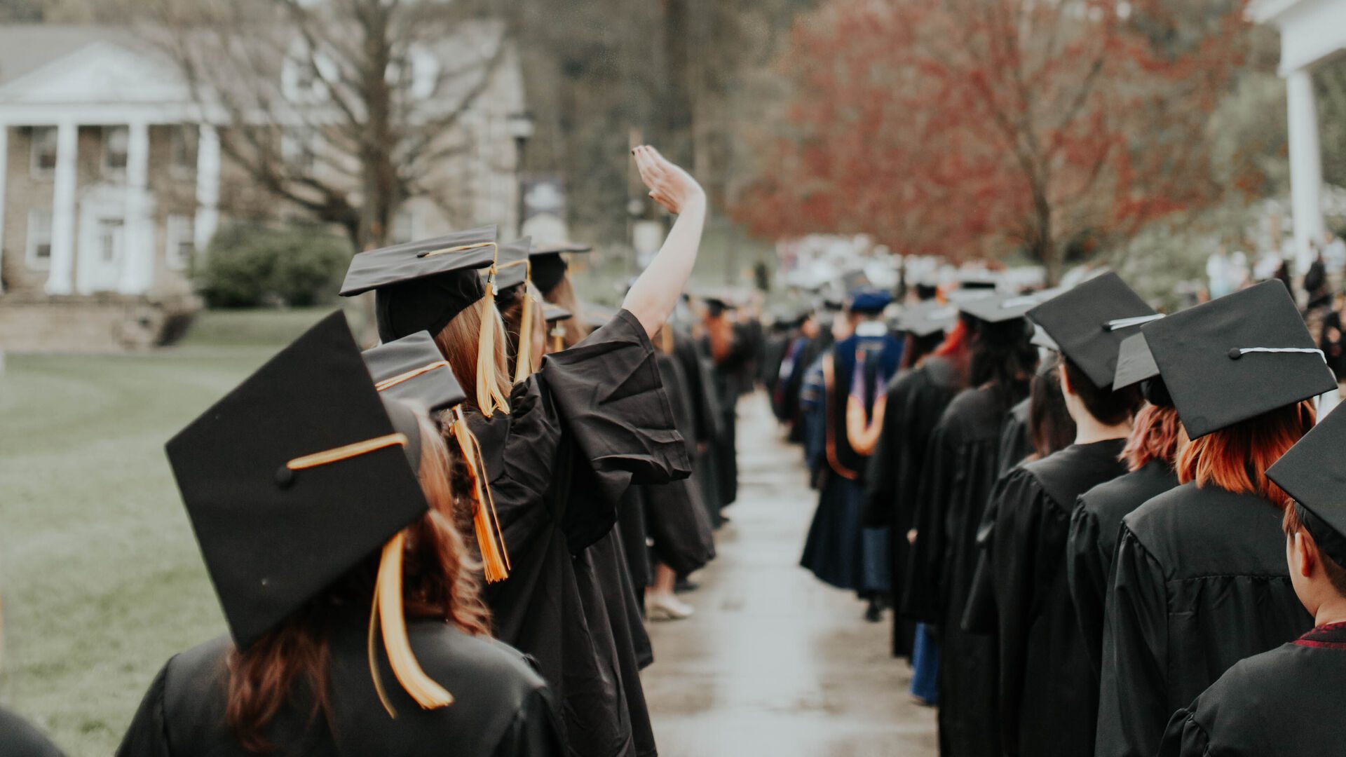 Two lines of Houghton graduates wearing regalia and caps on the campus lawn.