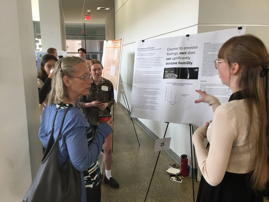 Female Houghton students presenting her poster to others