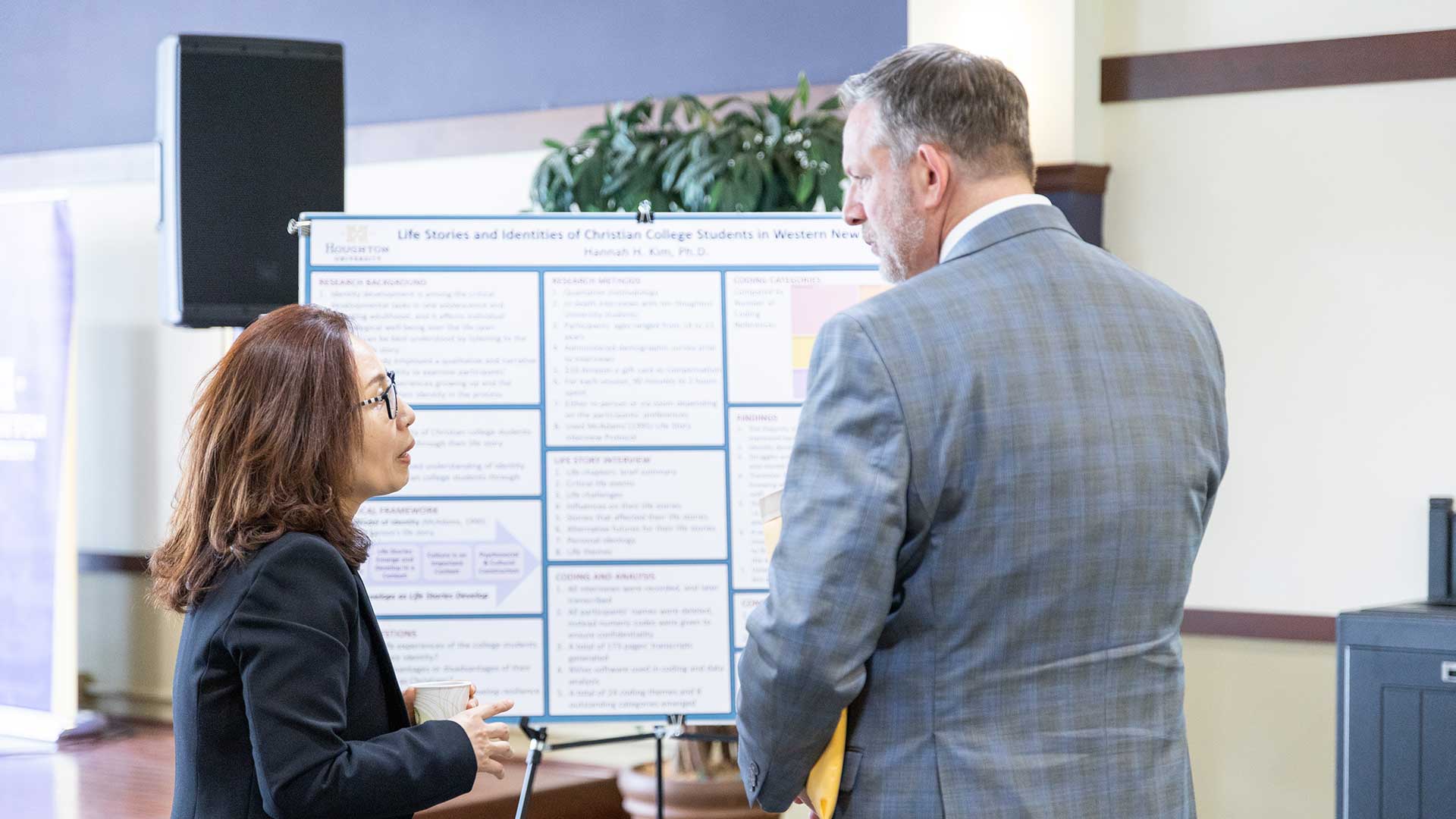 Two Houghton faculty looking at Faculty Scholarship Day poster.