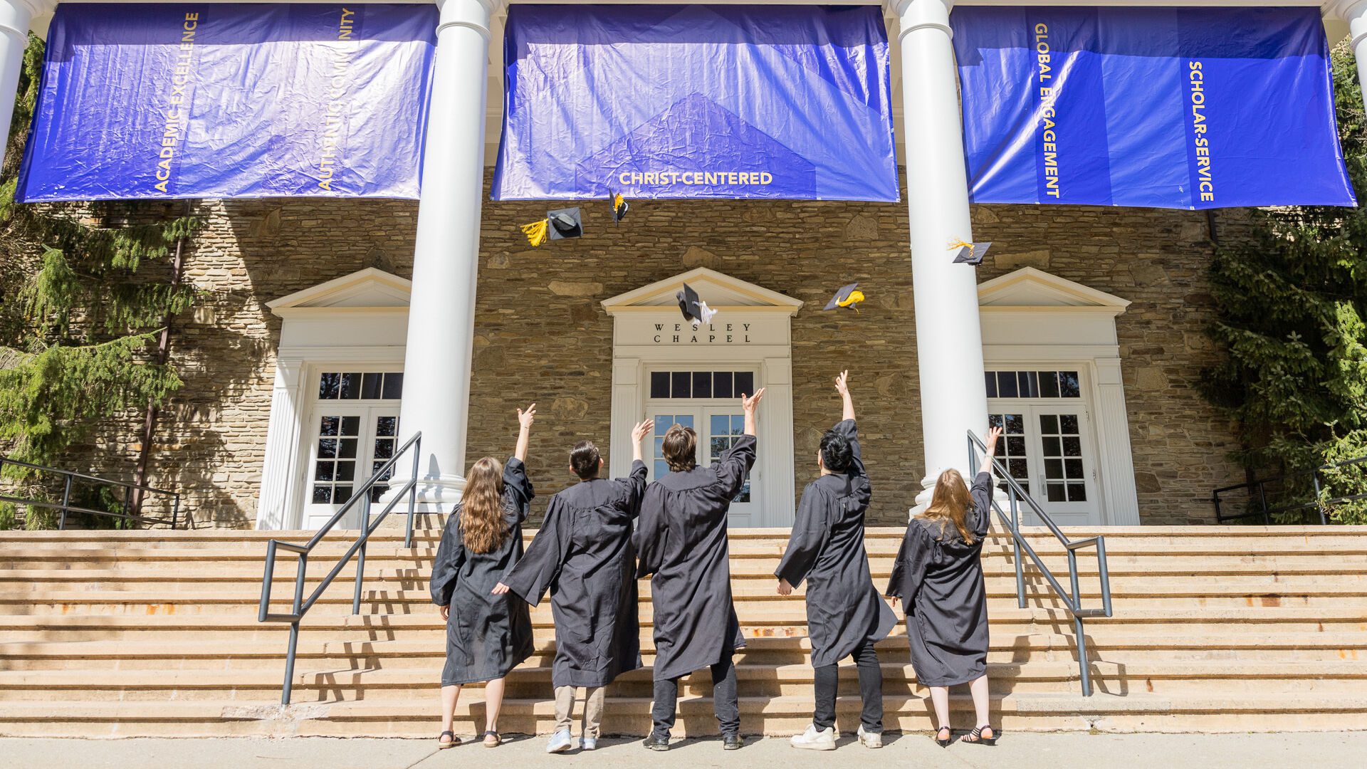 Houghton students throwing their graduation caps in the air on the steps of the Chapel.