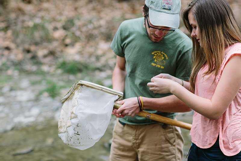 Two Houghton environmental science students looking at their findings from their net, standing in a river.