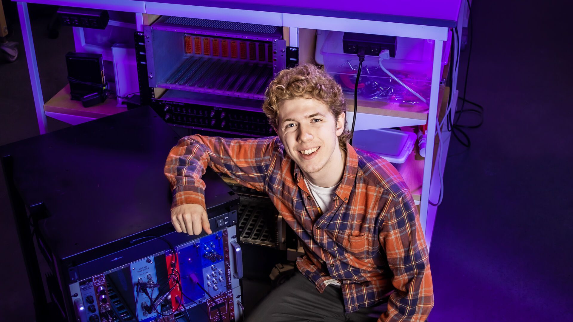 Houghton physics student Adam Brown next to equipment in lab.