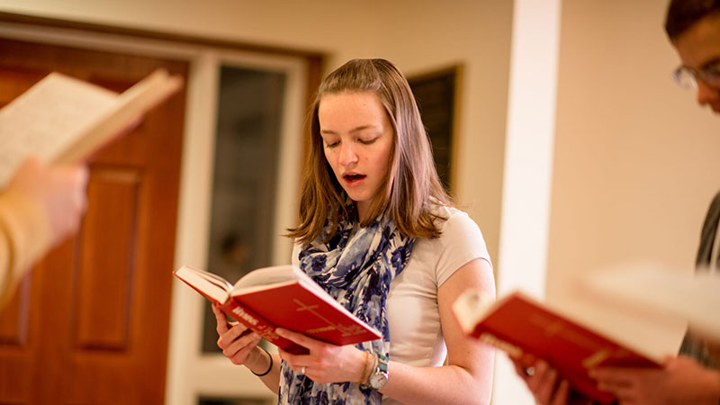 Houghton student singing from hymnal during communion service.