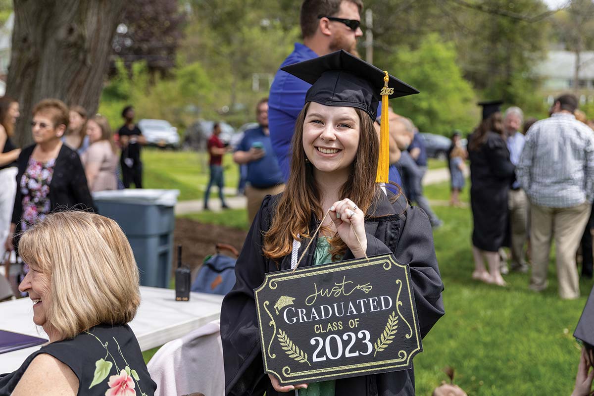 A recent Houghton graduate holding a sign that read, Just Graduated Class of 2023.