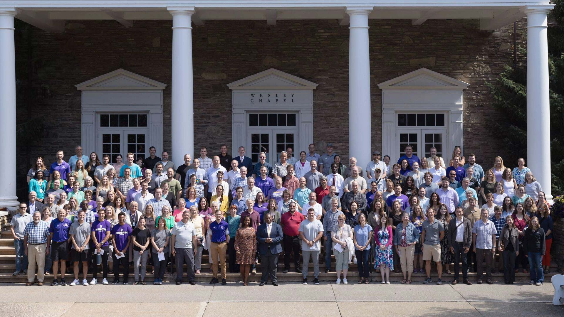 Houghton staff and faculty standing on the steps of the Wesley Chapel.