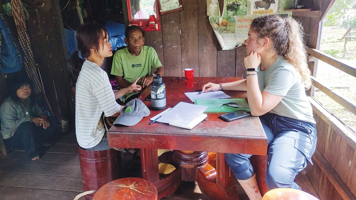 Houghton alumna Kelly Mohnkern sitting at table speaking with local residents in Cambodia.