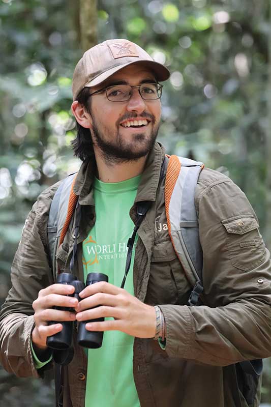 Kyle Burrichter standing with binoculars in the Cambodia jungle.