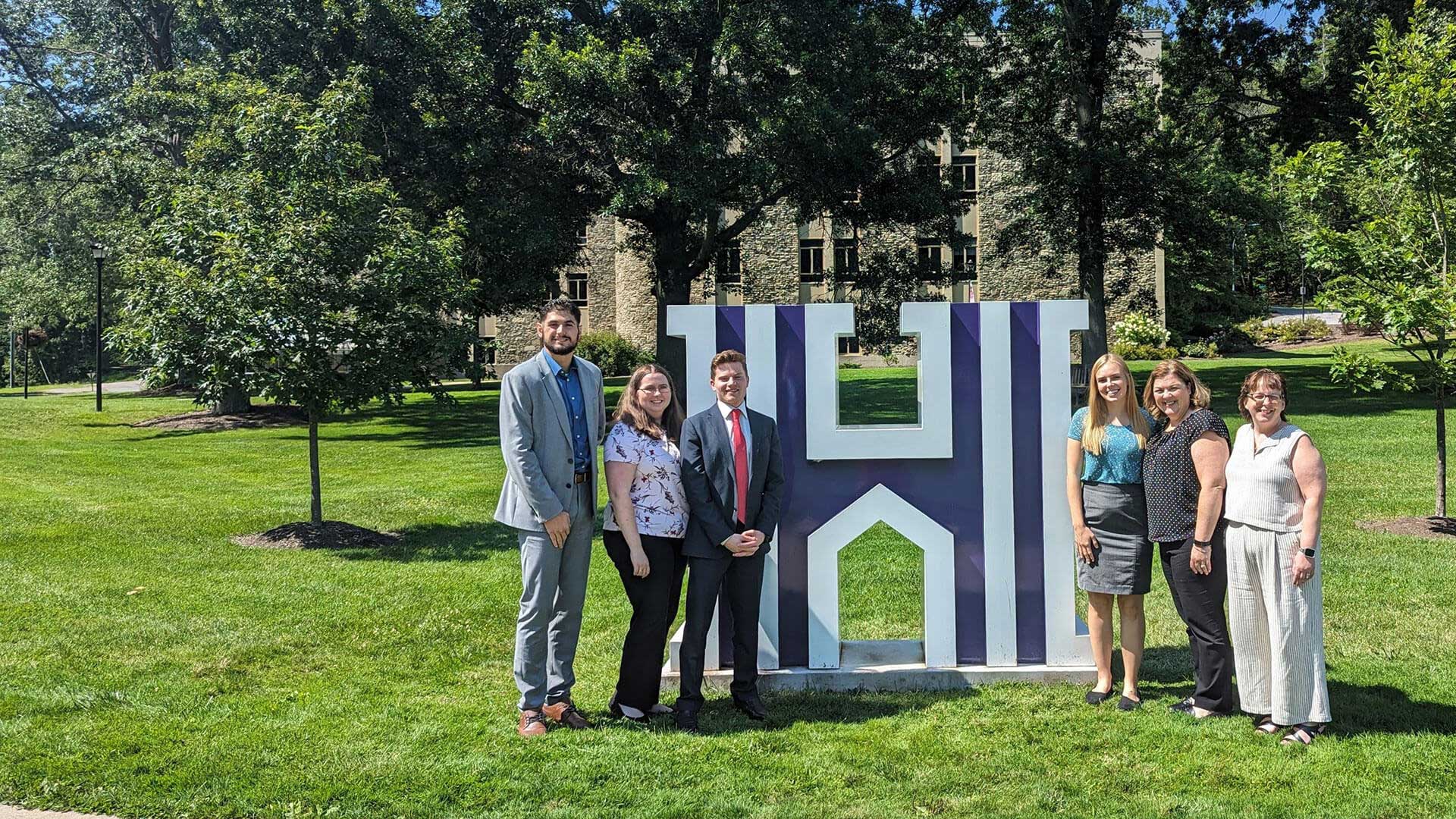 Houghton MBA residency students standing by the H on Houghton's campus.