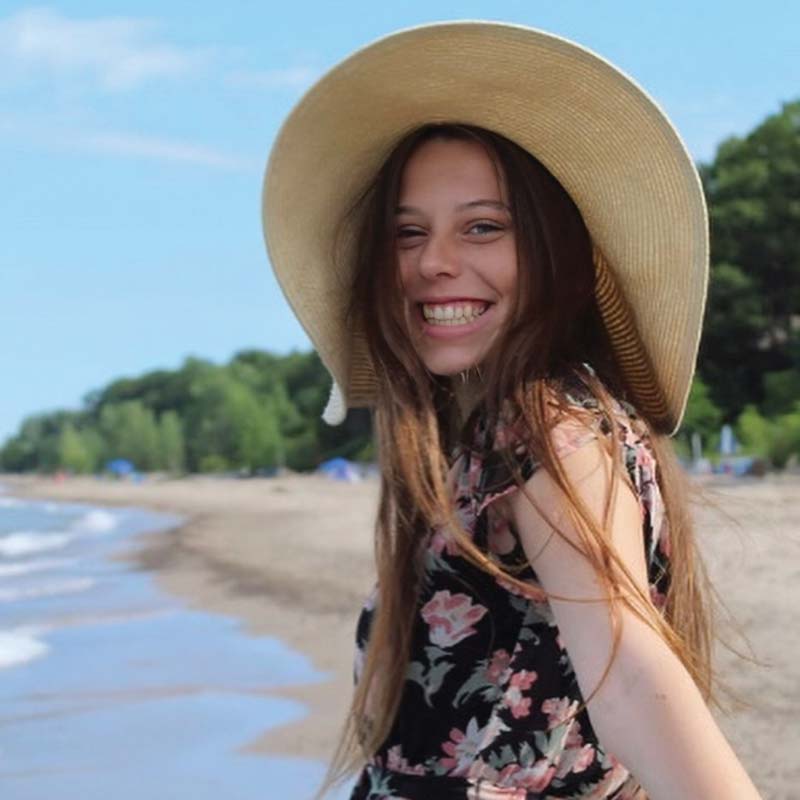 Houghton alumnus Rachel Caine standing on beach with large hat.