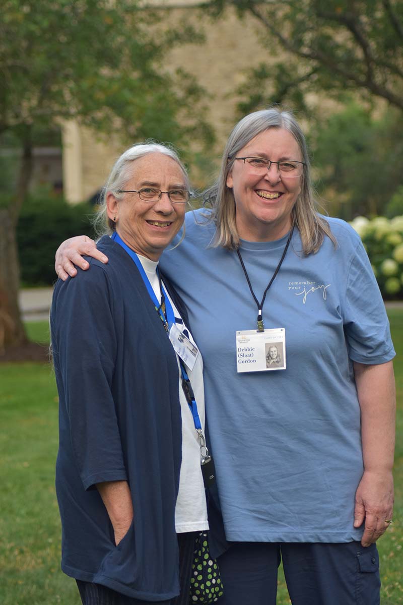 Two Houghton alumni standing on campus lawn smiling during summer alumni reunion.
