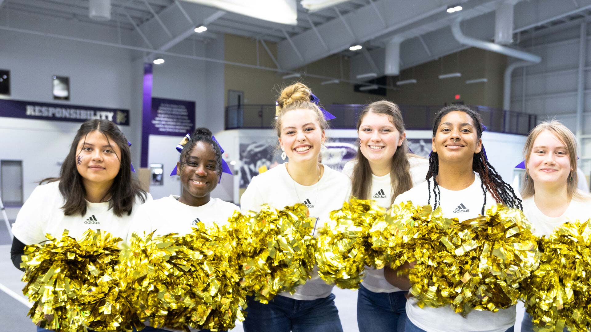Six Houghton students standing with shimmery gold pom poms during Homecoming weekend.