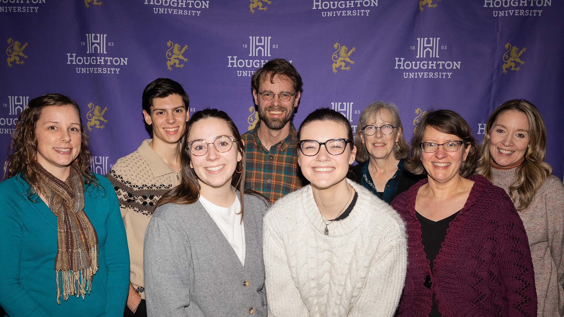 Houghton University's December graduates, along with some faculty and staff, smile for the camera in front of a Houghton banner