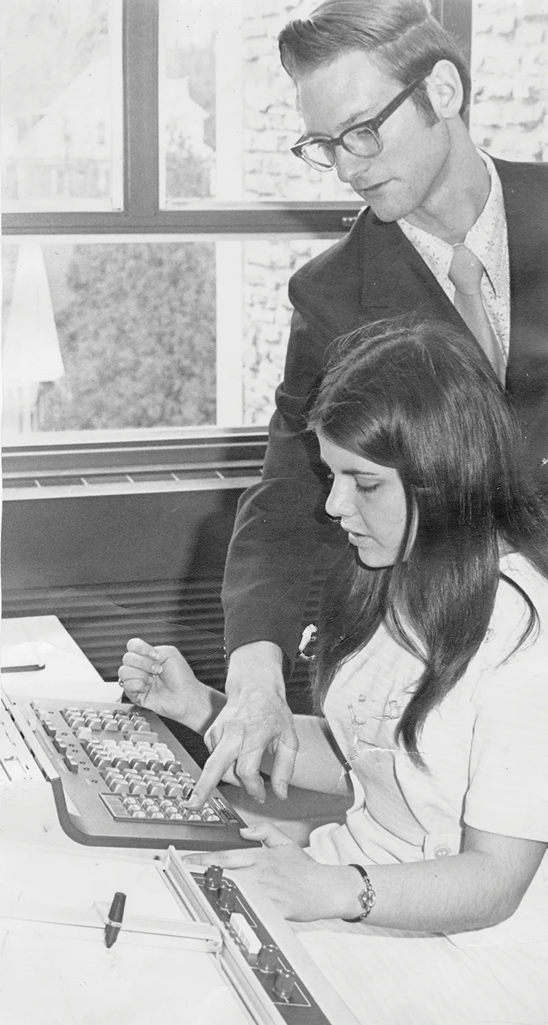 Archival black and white photo of student and professor with IBM computer.