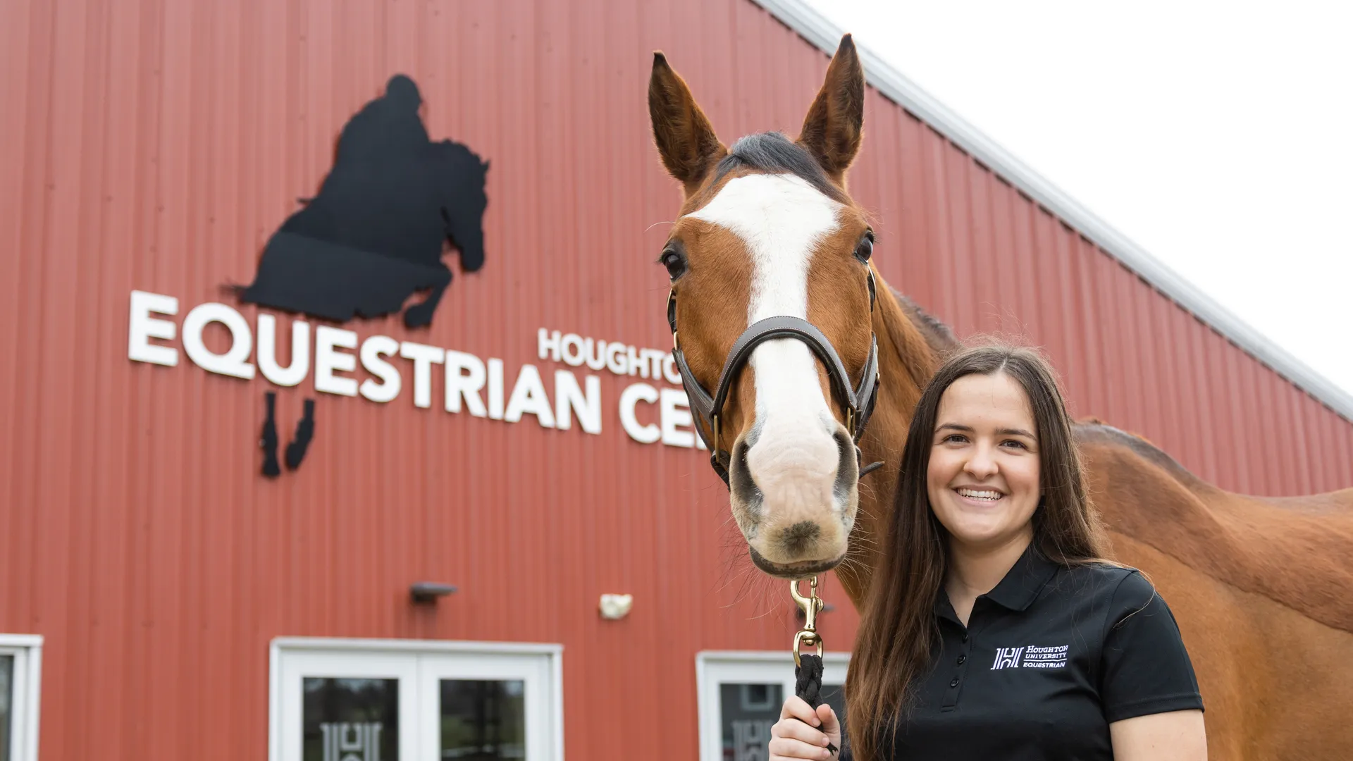 Houghton equestrian student Cassidy Kuhlmann standing with horse in front of equestrian center.