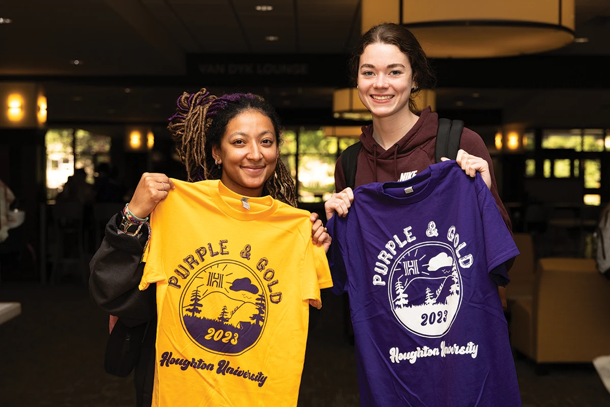Two Houghton students holding purple and gold shirts.