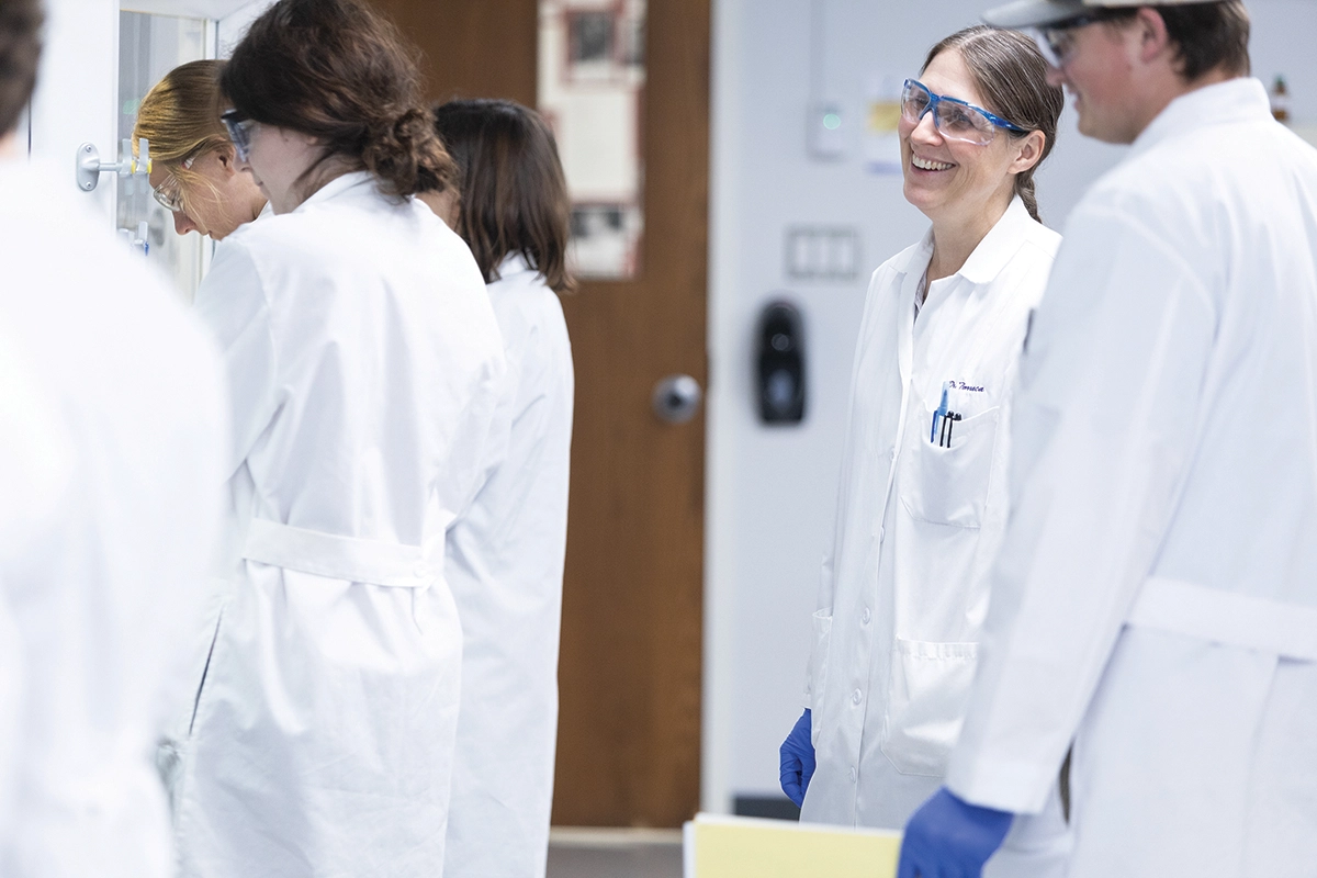 Houghton chemistry professor Dr. Karen Torraca working with students in lab wearing lab coats.