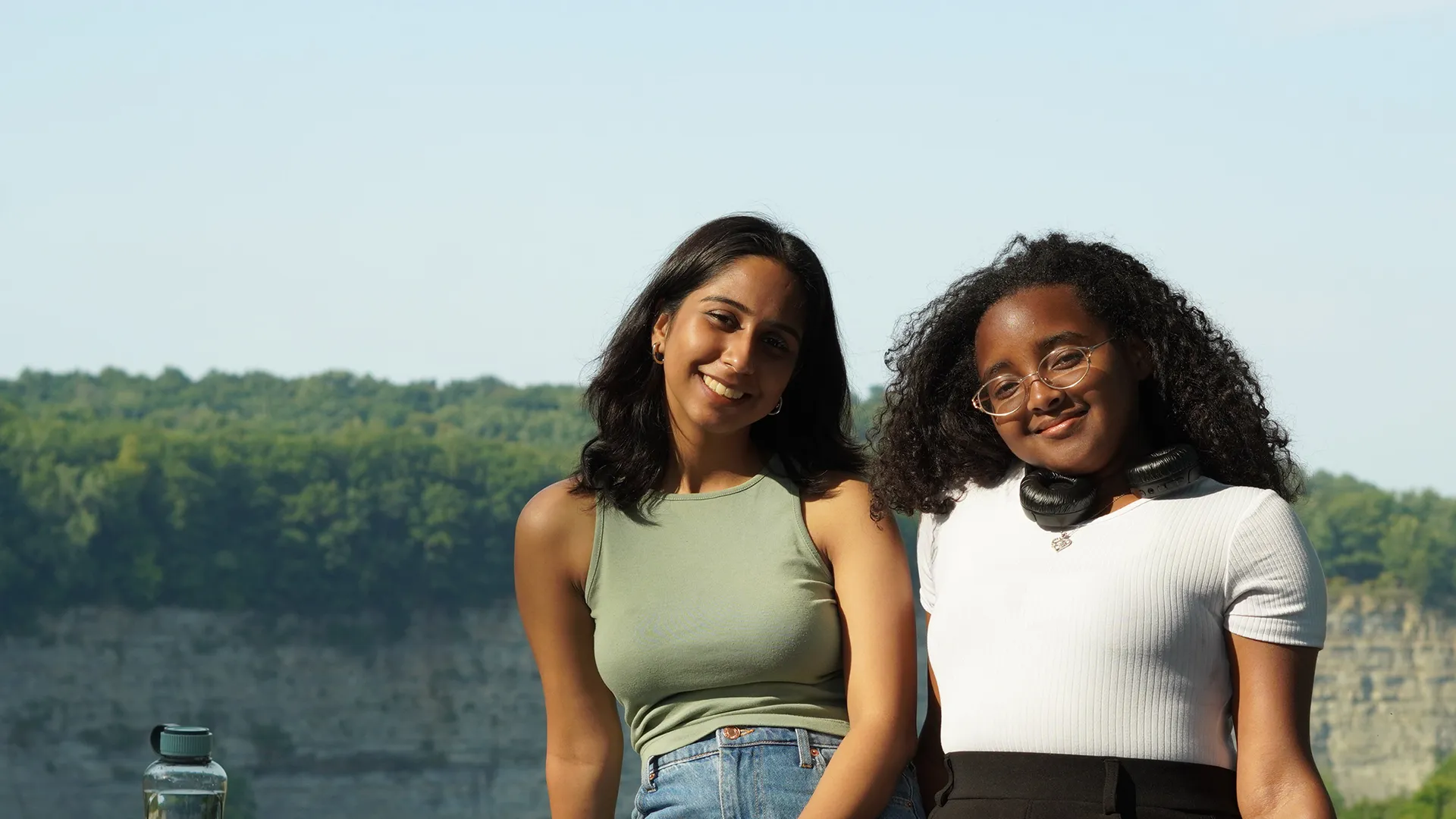 Two Houghton international interconnect students leaning against rock ledge in front of scenic vista.