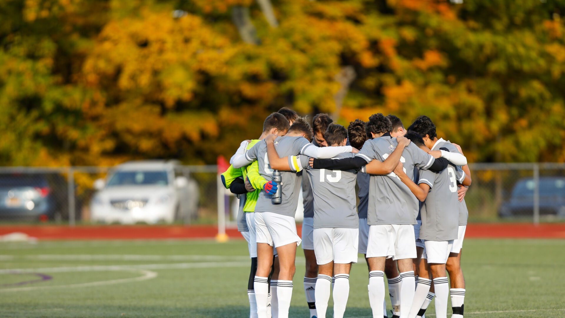 Houghton mens soccer team standing together in a huddle on the field.