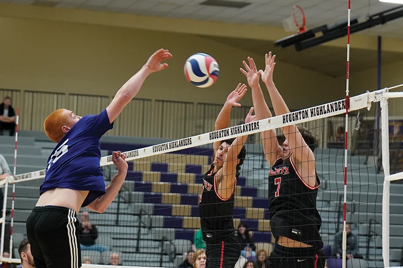 Houghton men's volleyball player hitting ball over net to opponents.
