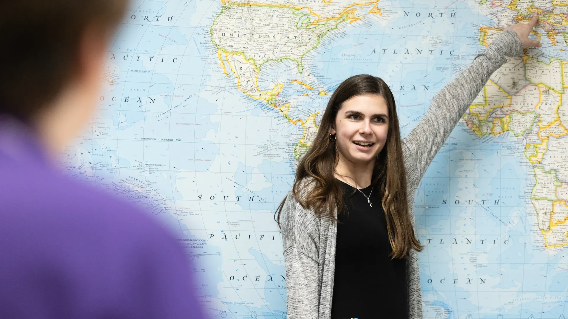 Houghton MAT degree student pointing at world political map as they teach in class.